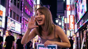 夜の歓楽街で、ネオンを背景に笑顔で客引きをする若い女性。